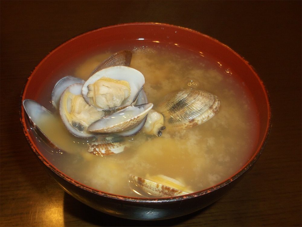 Schale Misosuppe mit geöffneten Venusmuscheln und Frühlingszwiebel