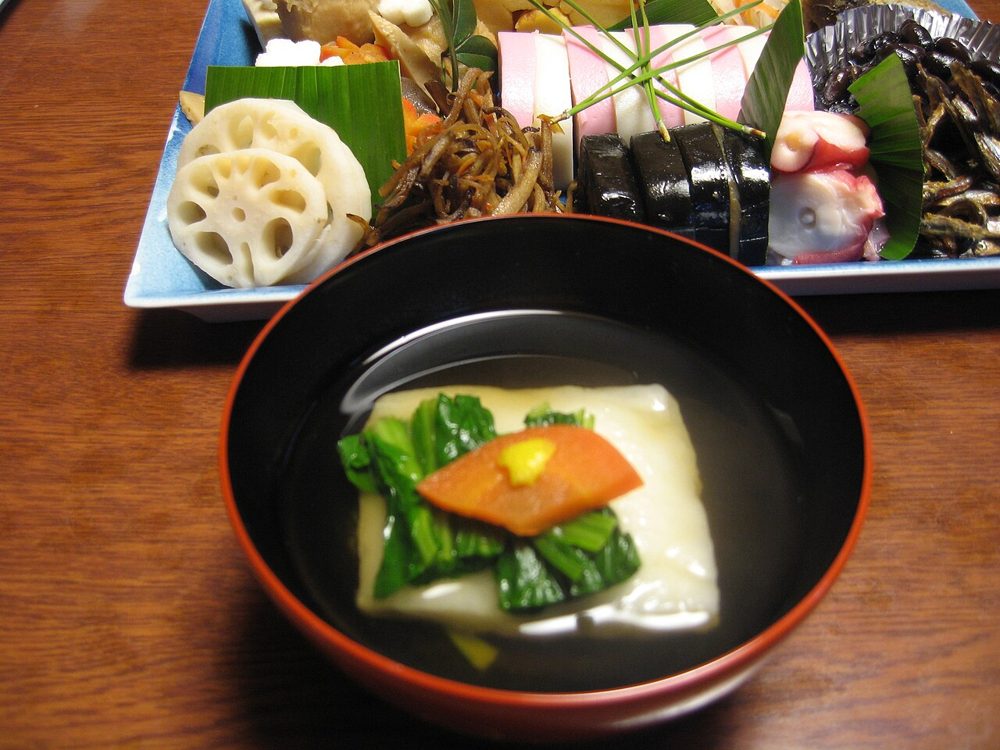 Schale Ozōni mit geröstetem Mochi, Hähnchen und Gemüse neben Osechi-Gerichten