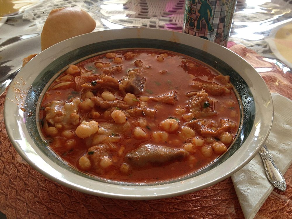 Schale roter Menudo mit Maiskörnern, Zwiebeln und Limette