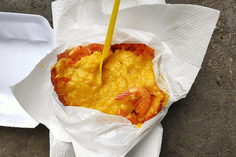 Aufgeschnittenes Acarajé, gefüllt mit Vatapá und Garnelen, in Papier