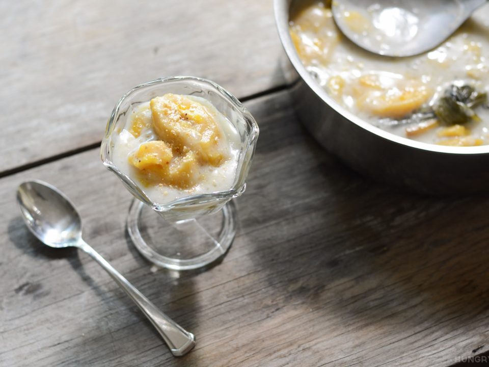 Glasschale mit Bananen in Kokoscreme, daneben ein Löffel