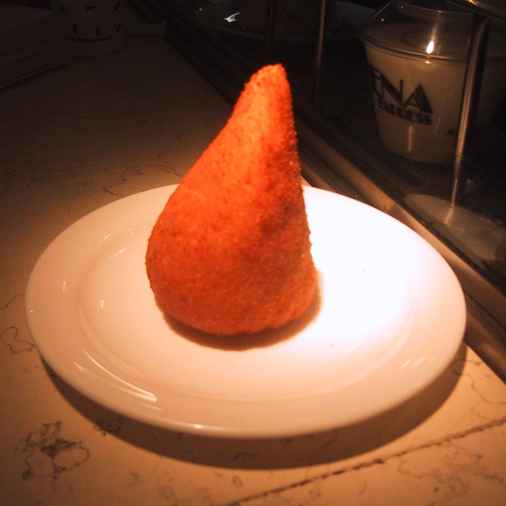 Einzelne goldbraune, tropfenförmige Coxinha auf einem weißen Teller
