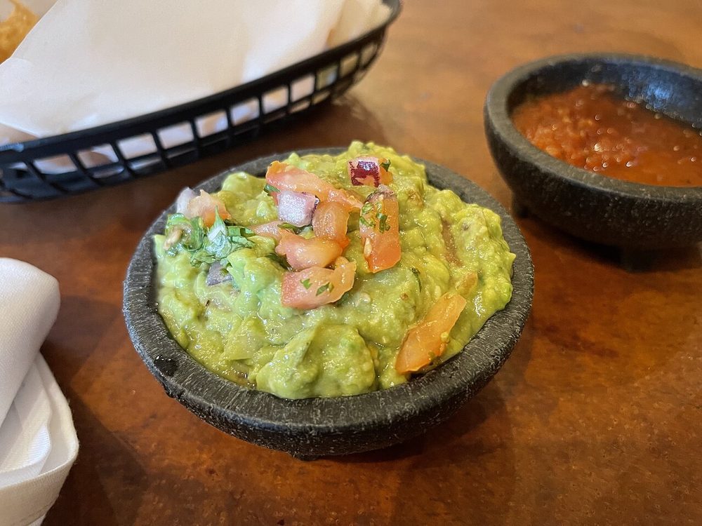Guacamole im Steinmörser, dahinter Salsa und Tortilla-Chips