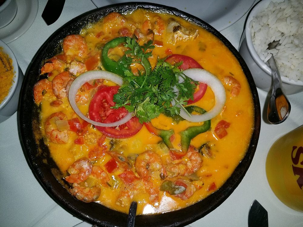 Moqueca in einer schwarzen Pfanne mit Garnelen, Tomaten- und Paprikaringen