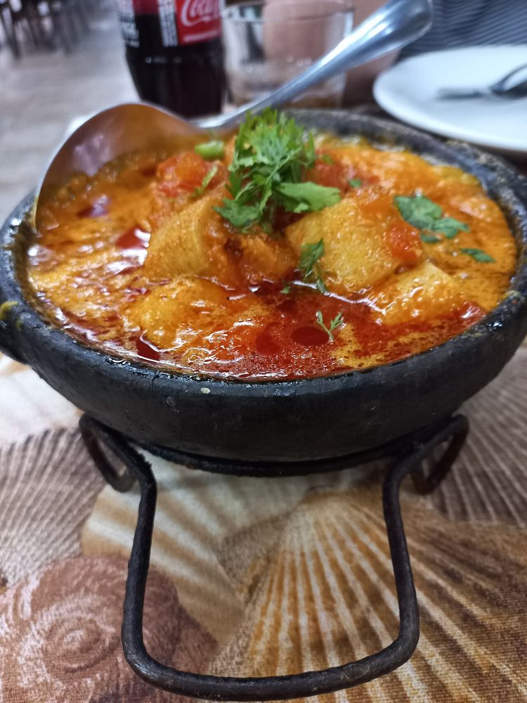 Schwarzer Tontopf mit Kochbananen-Moqueca in rotem Sud
