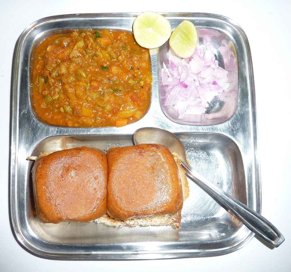 Pav Bhaji mit Brötchen, Zwiebeln und Zitrone auf einem Metalltablett