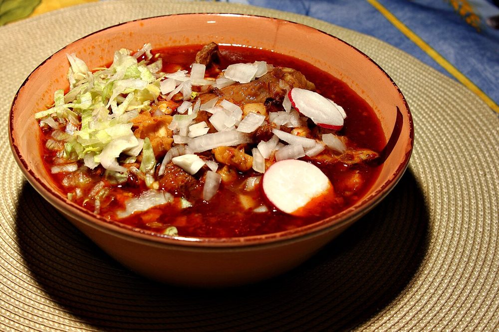 Schale mit rotem Pozole, garniert mit Salat, Zwiebel und Radieschen