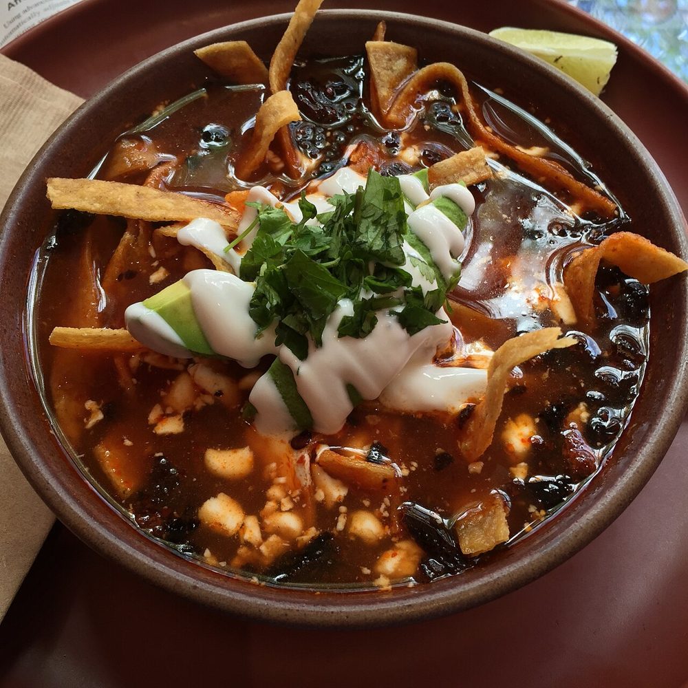Tonschale mit Tortillasuppe, Tortillastreifen, Käse und Koriander