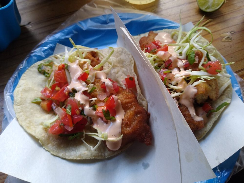Zwei Fisch-Tacos mit Pico de gallo und Sauce in einem Papierschiffchen